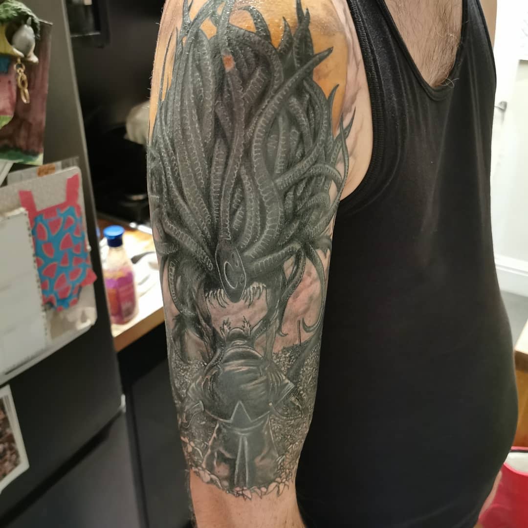 Upper arm tattoo depicting a Bloodborne hunter facing a massive, tentacled monster in detailed shading