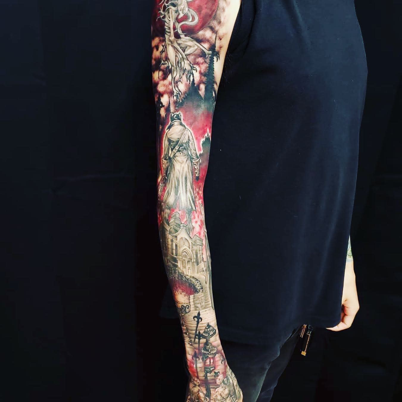 Full sleeve tattoo featuring a Bloodborne hunter in a gothic landscape, with vibrant red and black tones