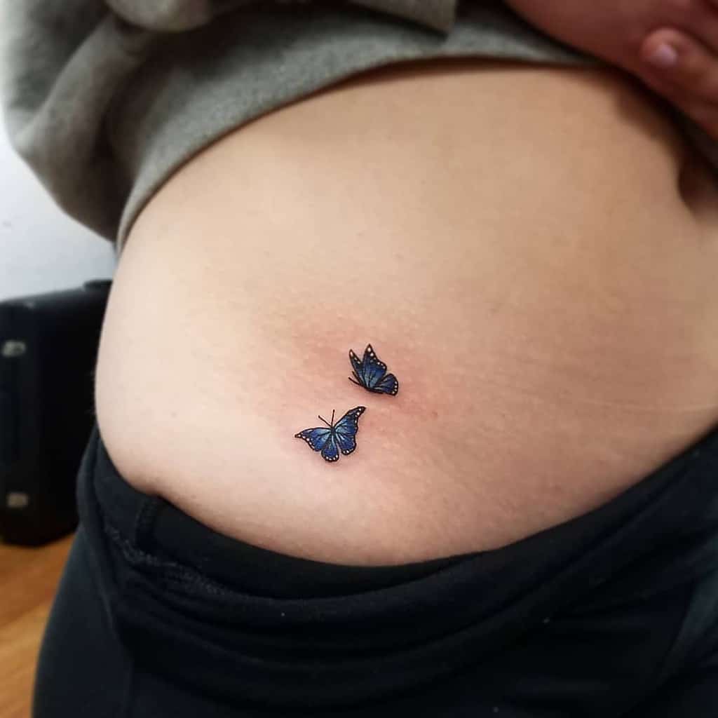Small and delicate blue butterfly tattoos on the hip, featuring fine details and subtle shading for a soft and elegant design.