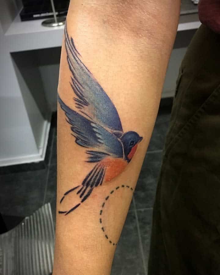 A tattoo of a colorful bird in flight on a forearm