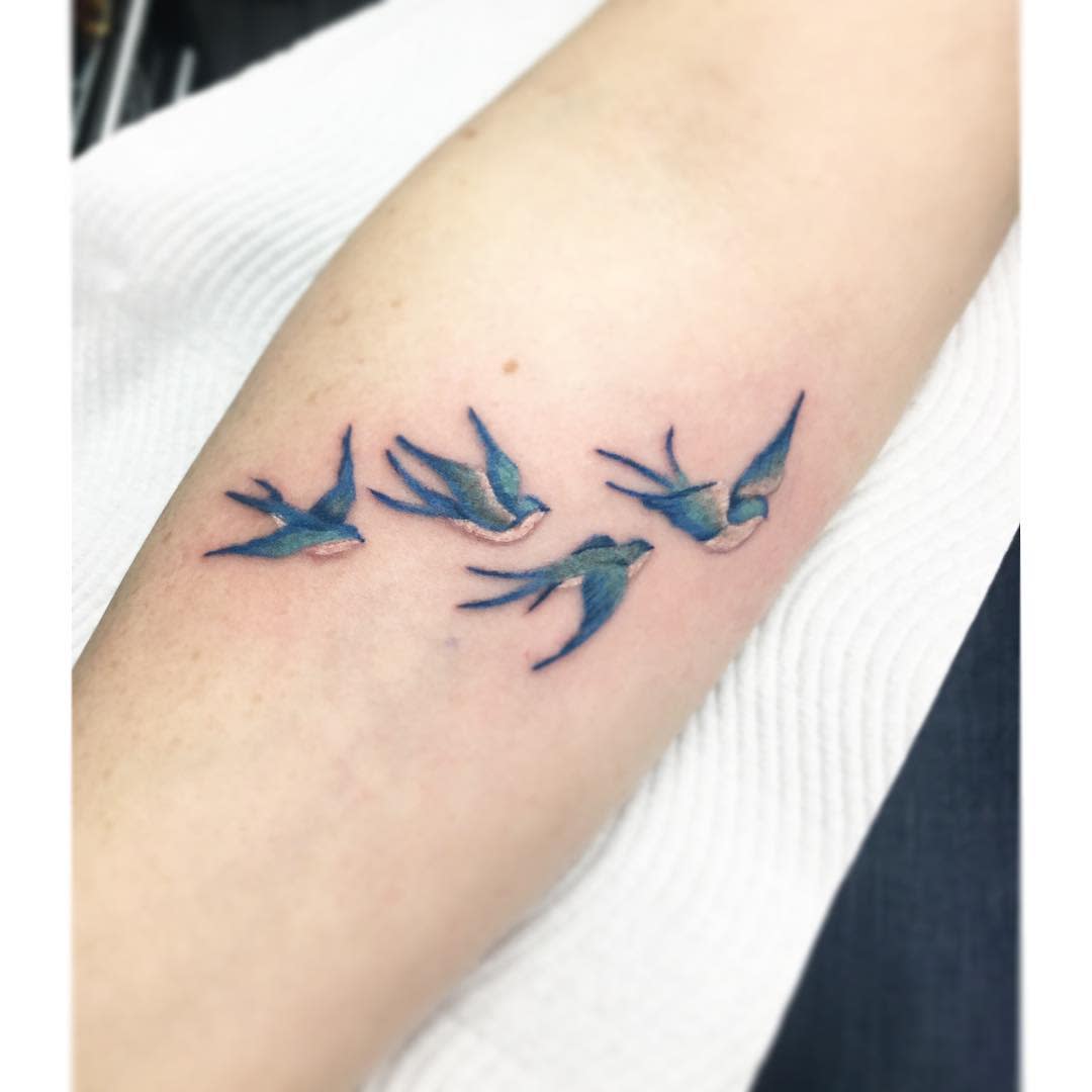 A tattoo of four blue and green birds in flight on a forearm