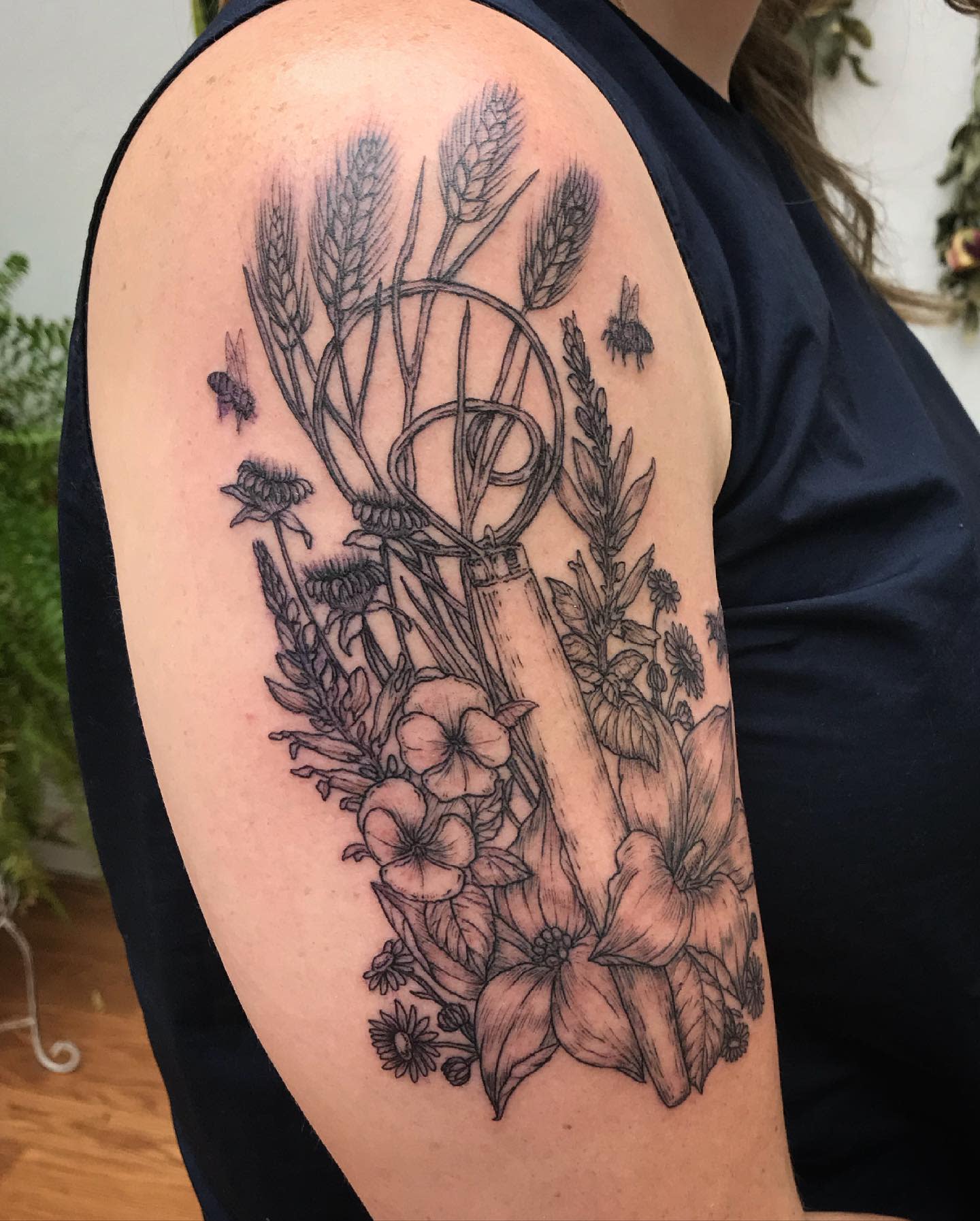 Arm tattoo featuring flowers, wheat, and bees surrounding a garden tool