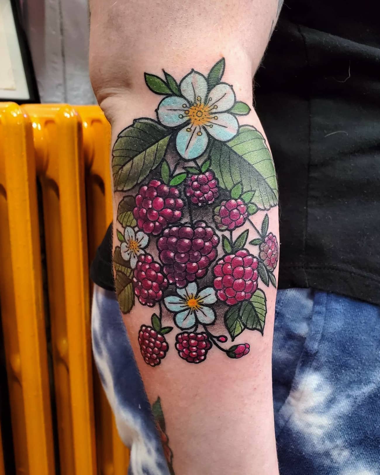 Arm tattoo featuring a bunch of raspberries, leaves, and a white flower