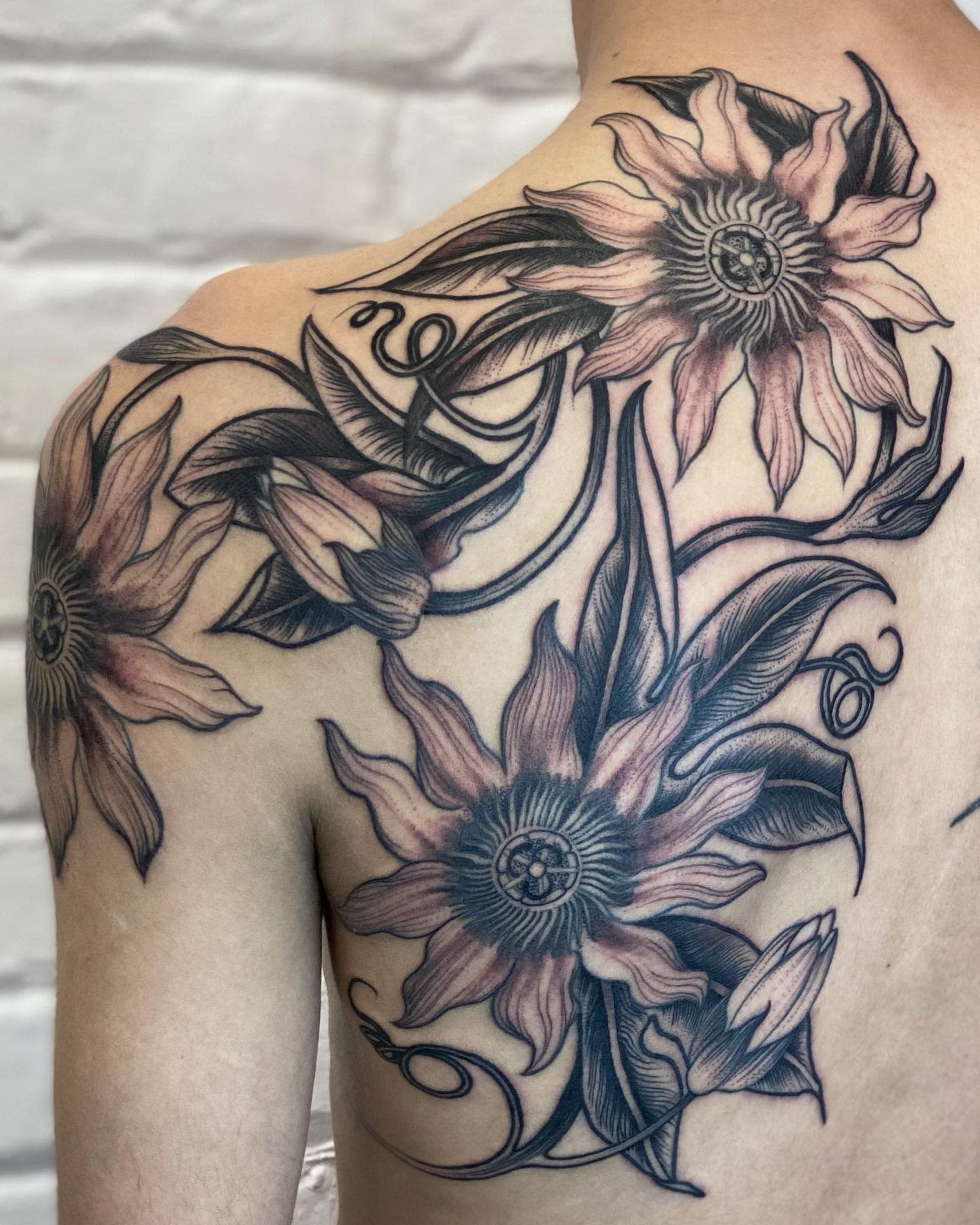 Tattoo of several large flowers and vines covering a shoulder and upper back