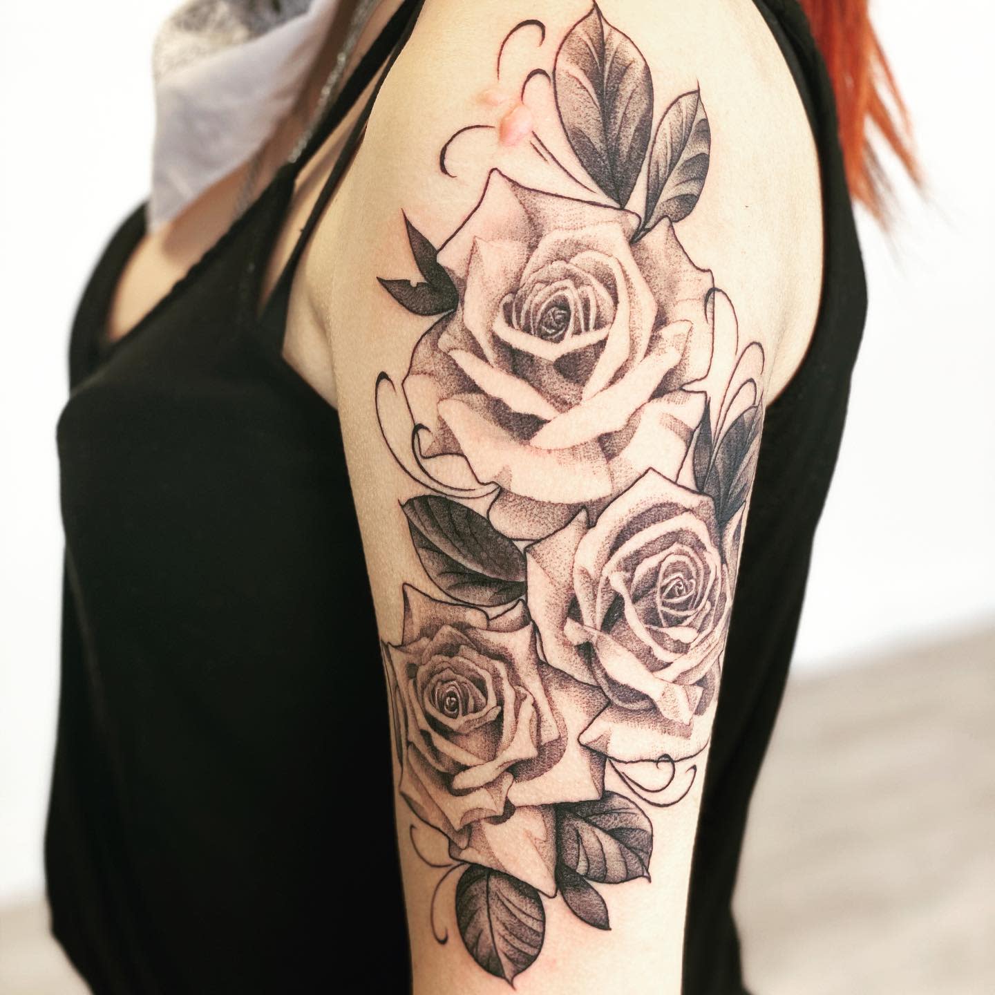 Black and grey rose tattoo sleeve on an arm with intricate shading and leaf details