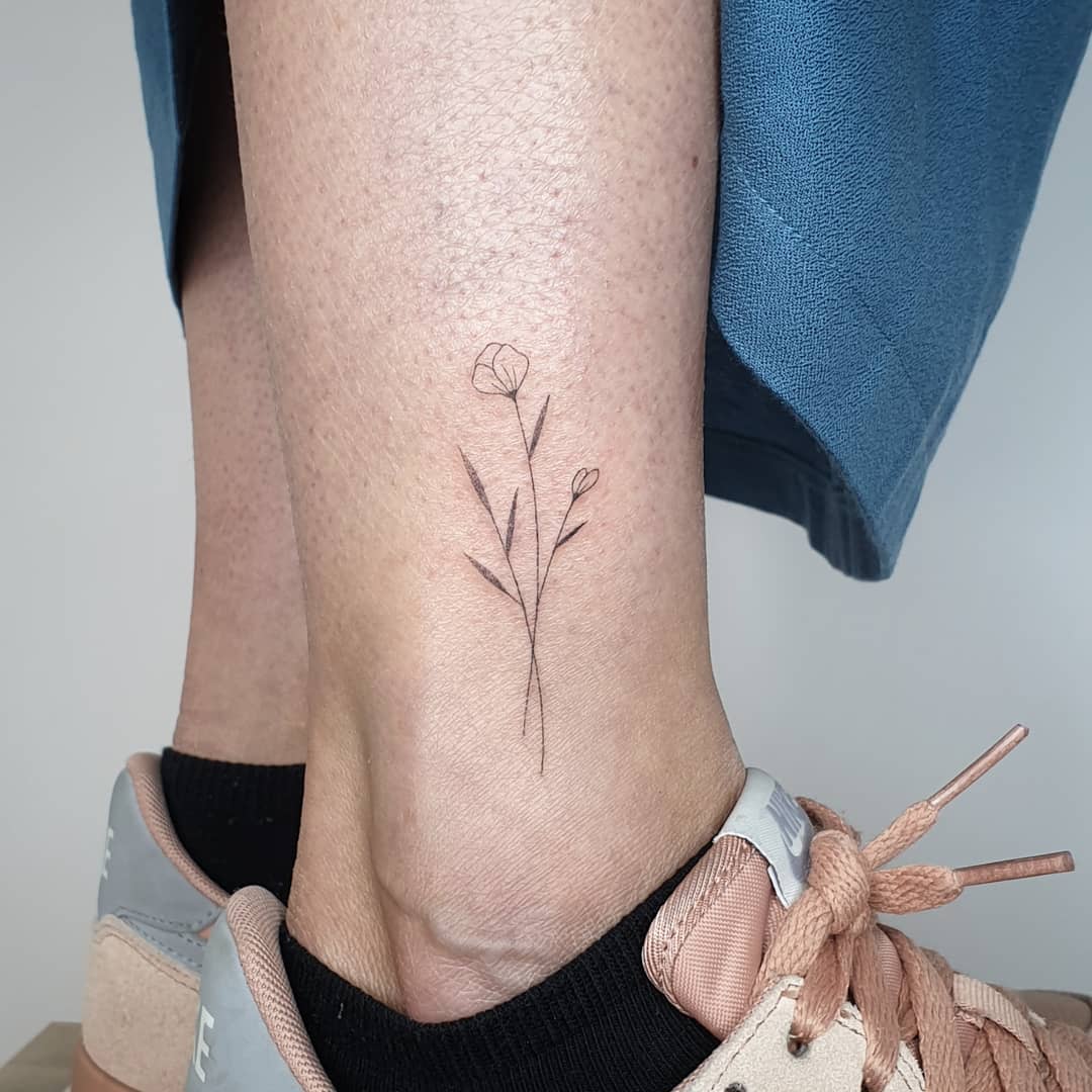 Delicate flower tattoo on an ankle with blue pants and pink sneakers visible