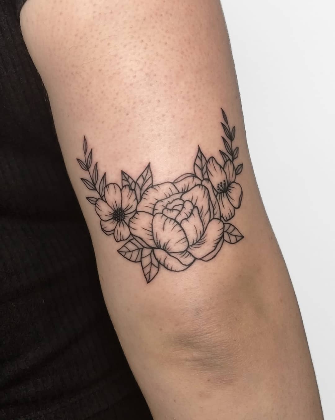 Black ink floral tattoo on upper arm, featuring a rose and smaller flowers
