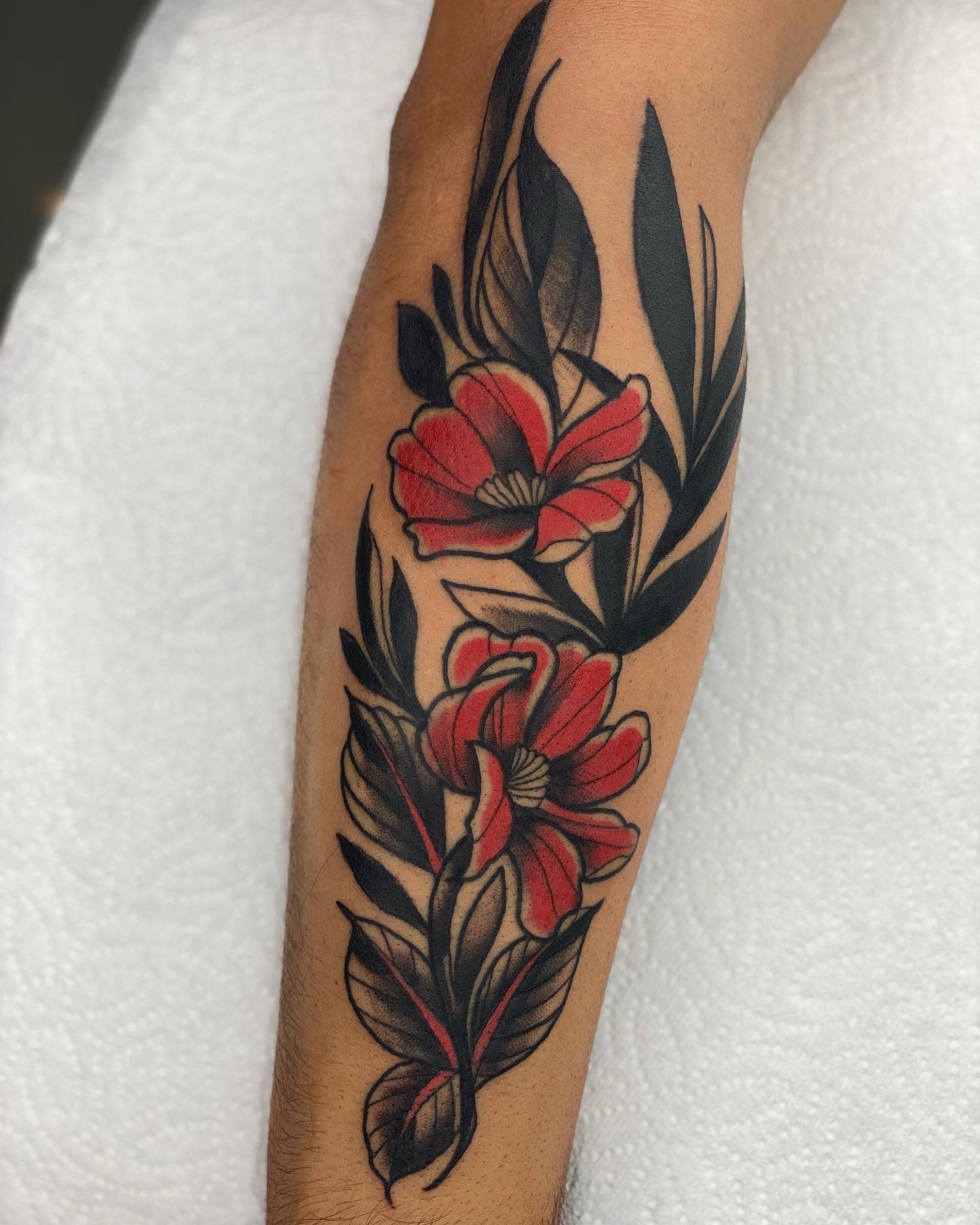 Forearm tattoo featuring red flowers with dark leaves