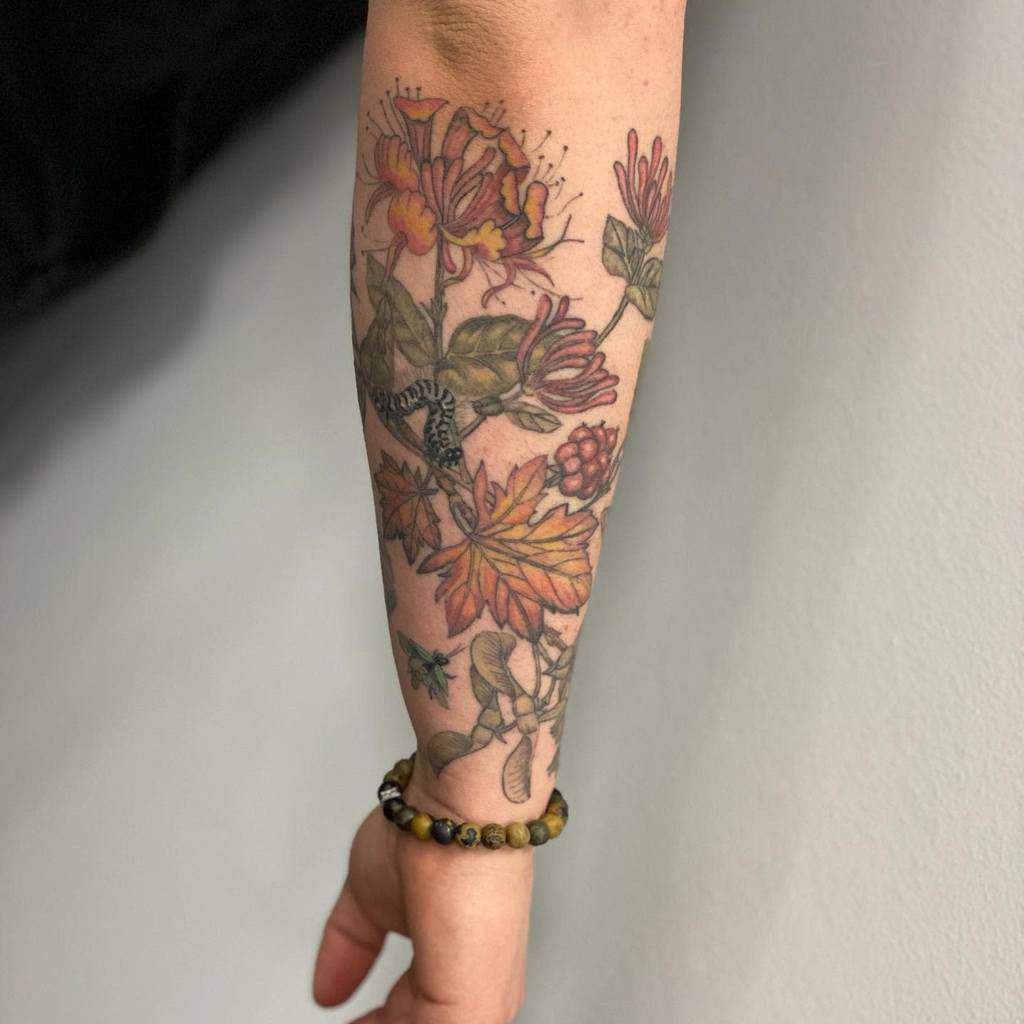 Forearm tattoo with colorful honeysuckle, leaves, and a small worm for a nature-inspired design