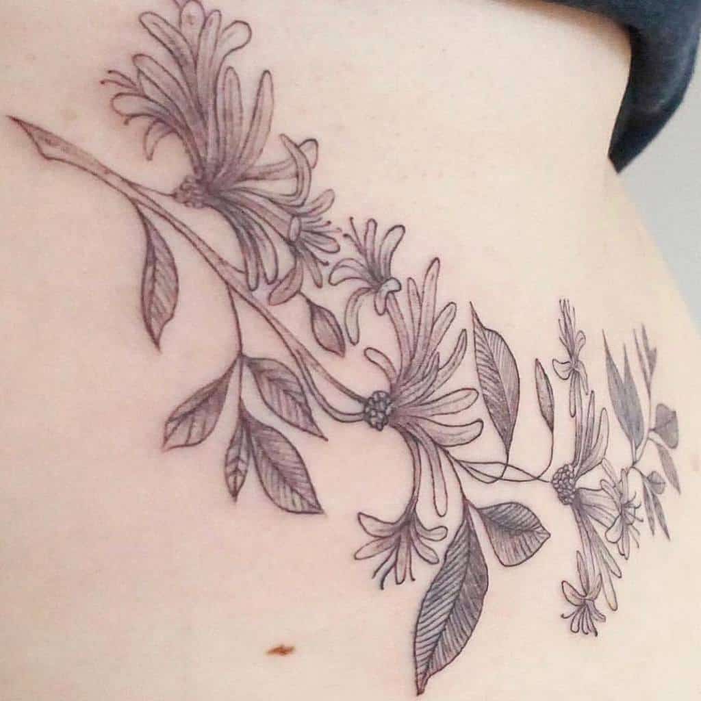 Delicate honeysuckle tattoo with soft, fine lines and flowing vines across the ribcage