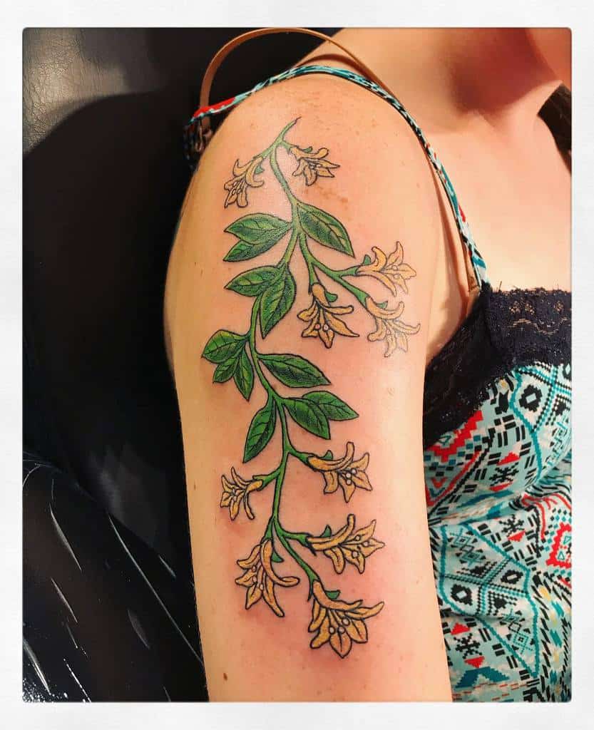Colorful upper arm tattoo featuring a long vine of honeysuckle with yellow blossoms and lush leaves