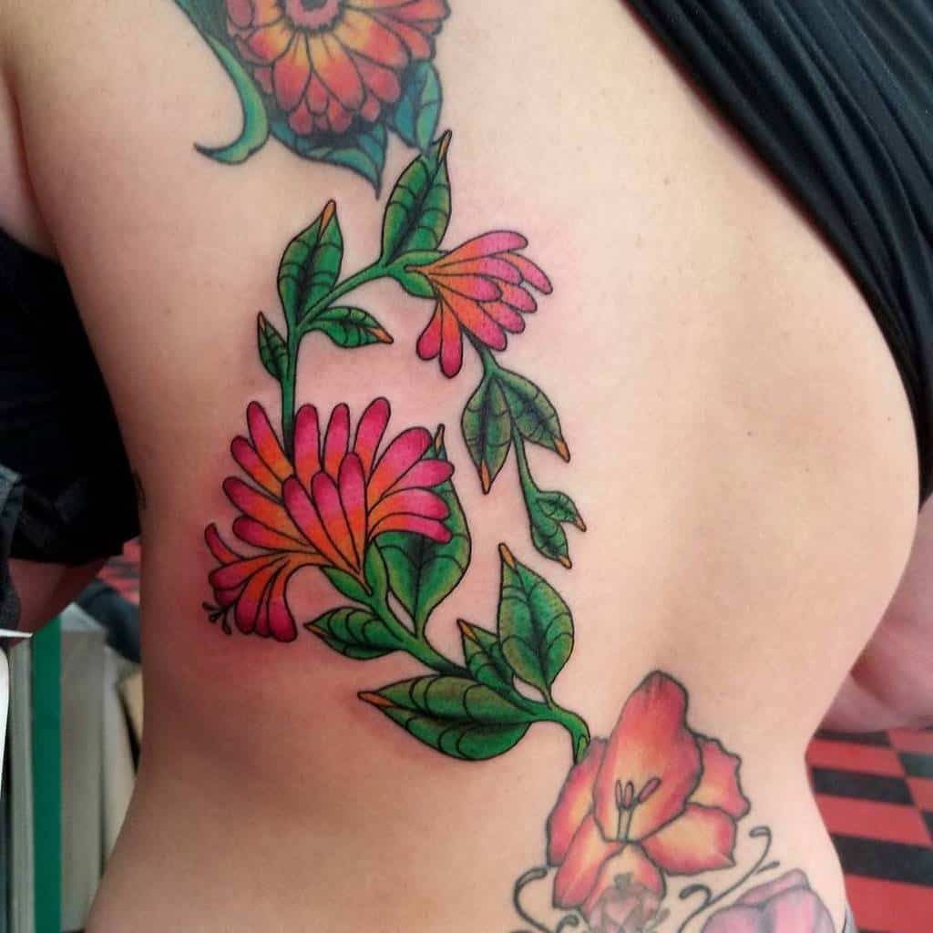Bold back tattoo with vibrant pink and green honeysuckle flowers and leaves flowing down the spine