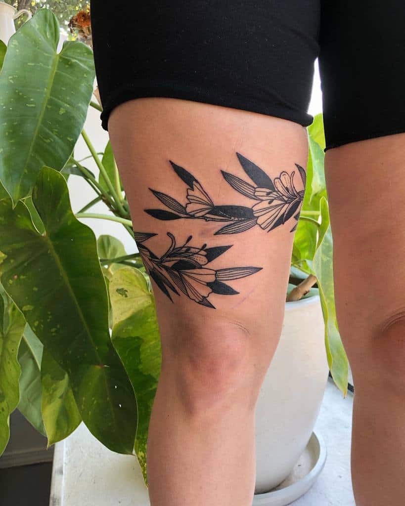 Elegant honeysuckle tattoo design on the thigh, with dark leaves and clean, simple flowers