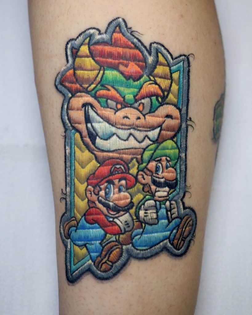 Stitch-inspired tattoo of Mario and Luigi karting away from a fierce Bowser, mimicking the look of an embroidered patch.