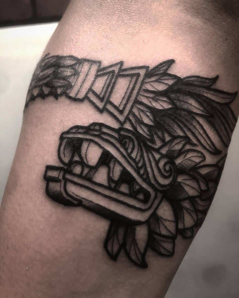 Black ink tattoo of a stylized Quetzalcoatl, featuring intricate feather and serpent details