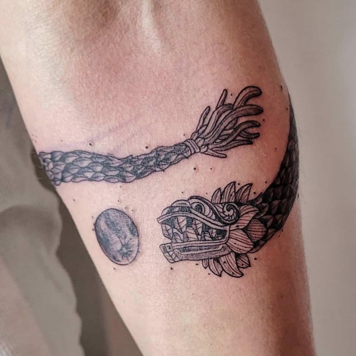 Detailed Quetzalcoatl tattoo with a braided serpent body and circular symbol, wrapping around the arm