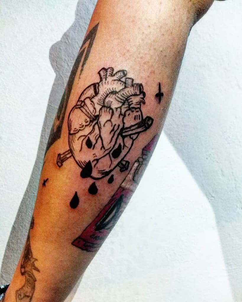 Tattoo of an anatomical black heart with nails and black drops