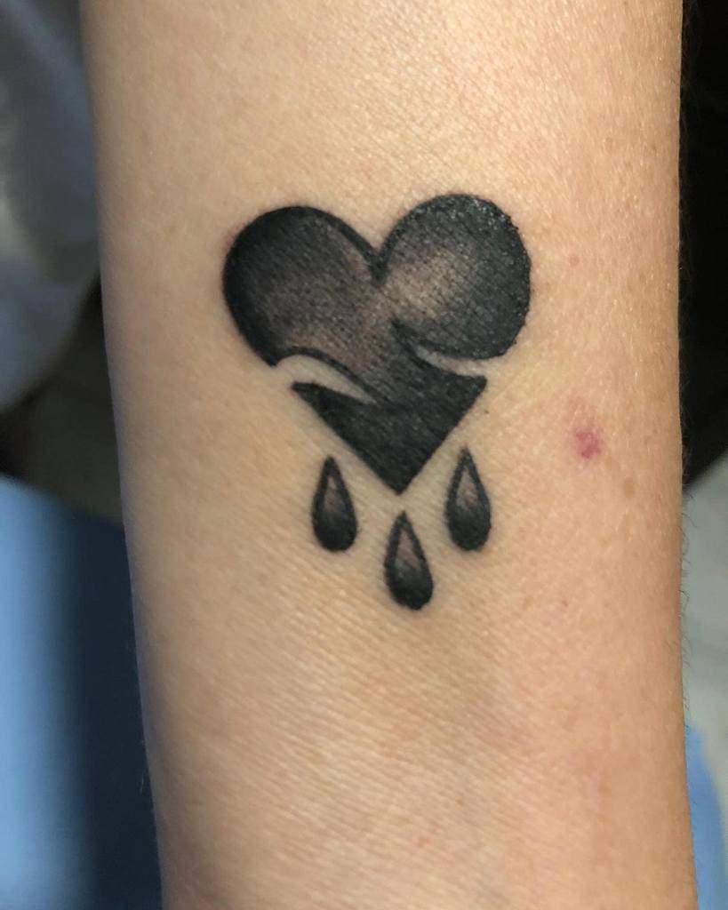 Tattoo of a black heart with three tear-shaped droplets below it