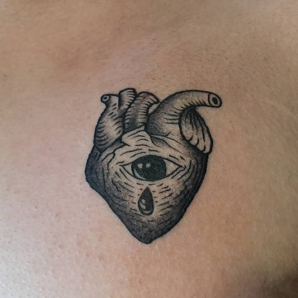 Tattoo of an anatomical black heart with an eye and a teardrop in black ink