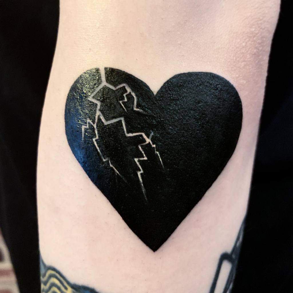 Tattoo of a black heart with jagged lightning bolt designs symbolizing a crack on the heart