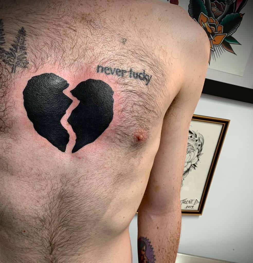 Large black heart tattoo split in two with 'never lucky' written beside it, expressing a sense of heartbreak and fate