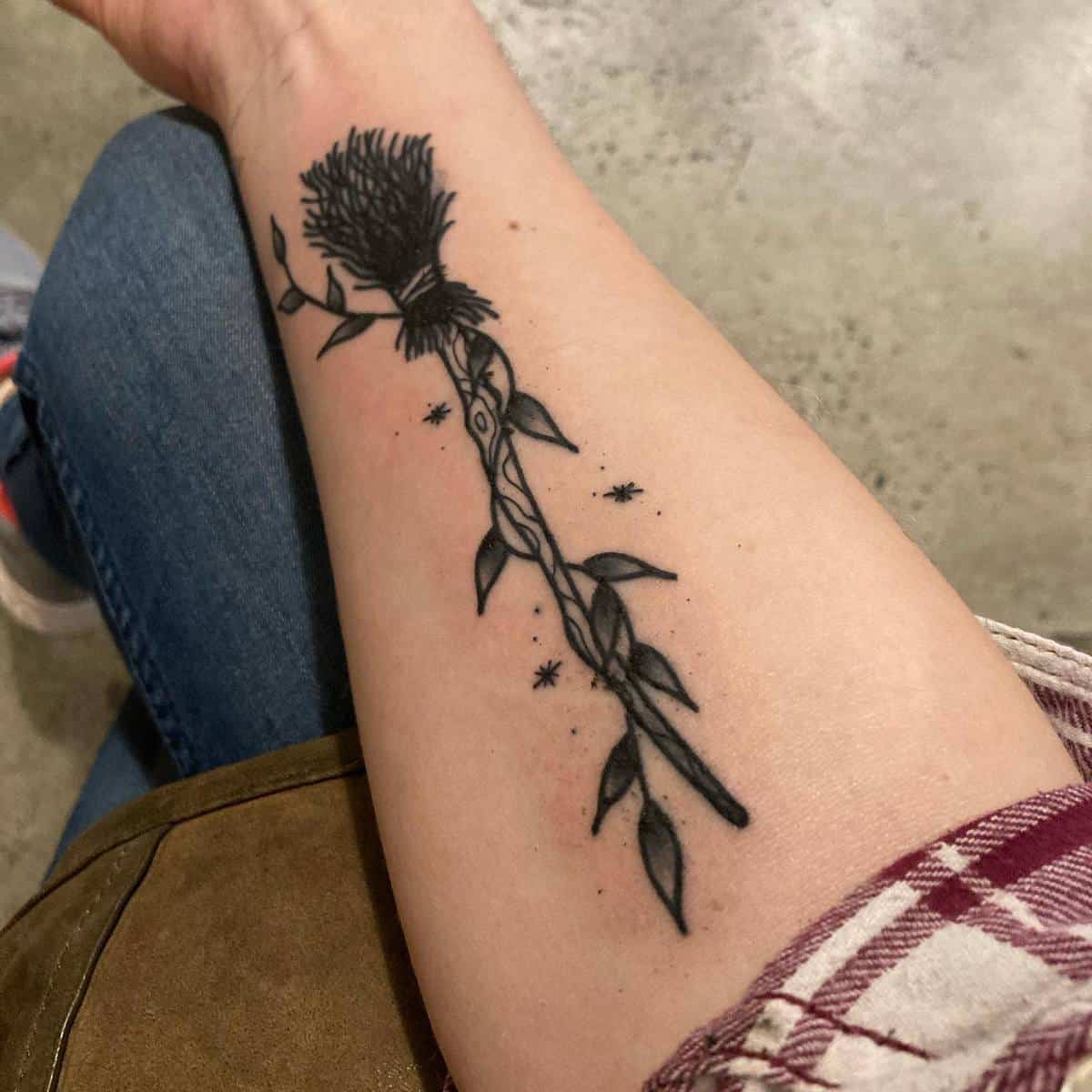 A forearm tattoo of a stylized broomstick with stars around it