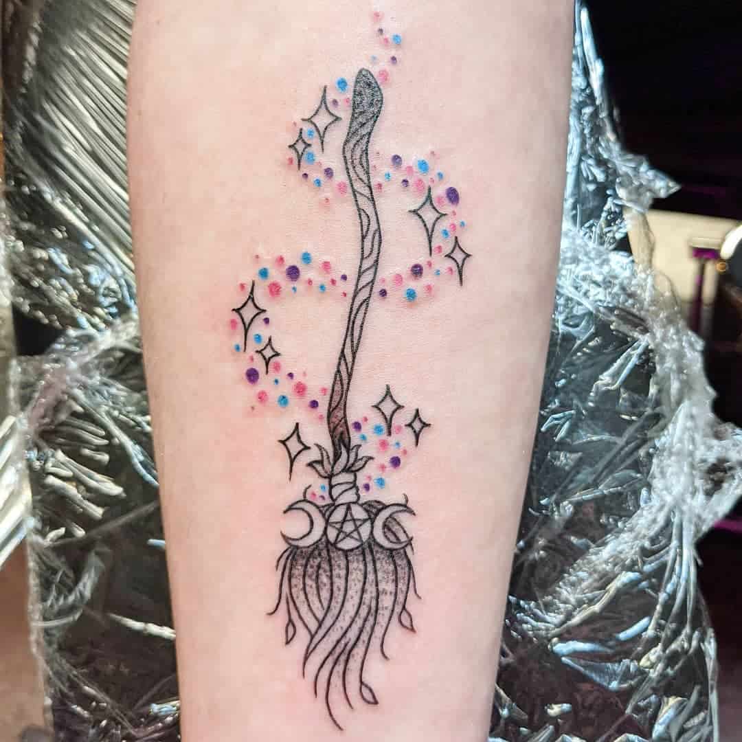 Tattoo of a broomstick with moons, stars, and sparkles on an arm