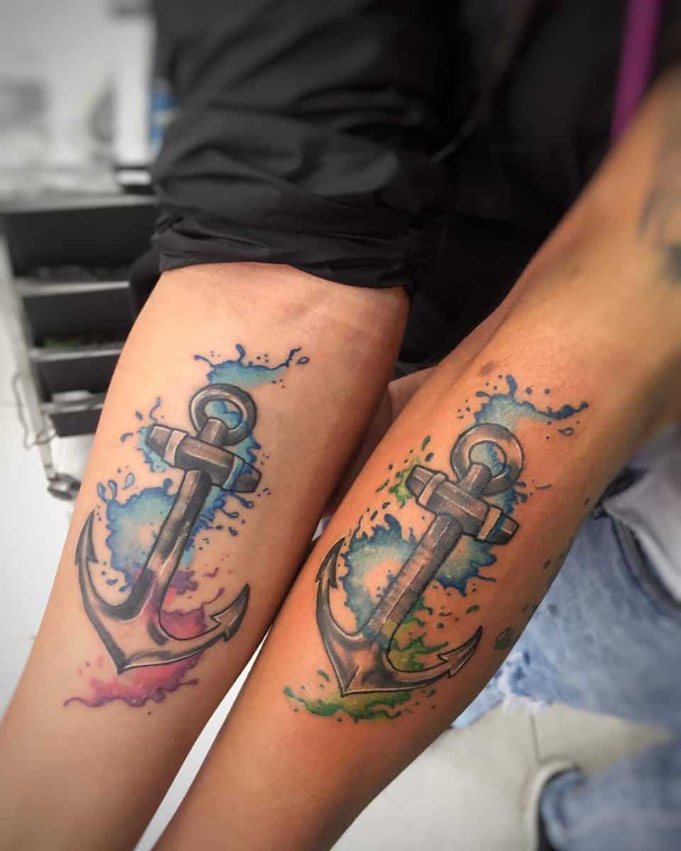 Matching anchor tattoos on forearms with colorful watercolor splashes
