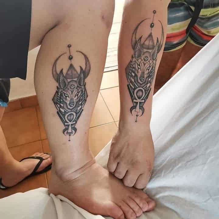 Matching geometric wolf tattoos on two people's calves