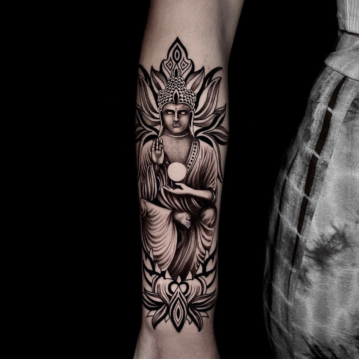 Buddha tattoo with lotus designs on an outstretched forearm