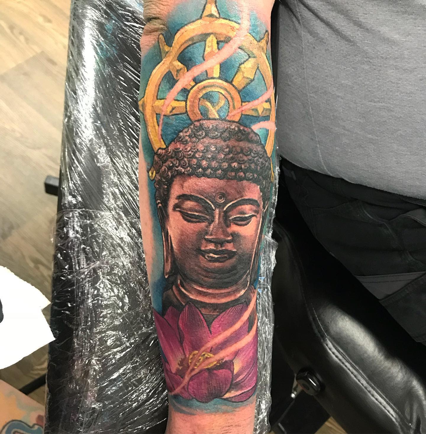 Tattoo of a serene Buddha with a lotus flower on the forearm featuring vibrant colors