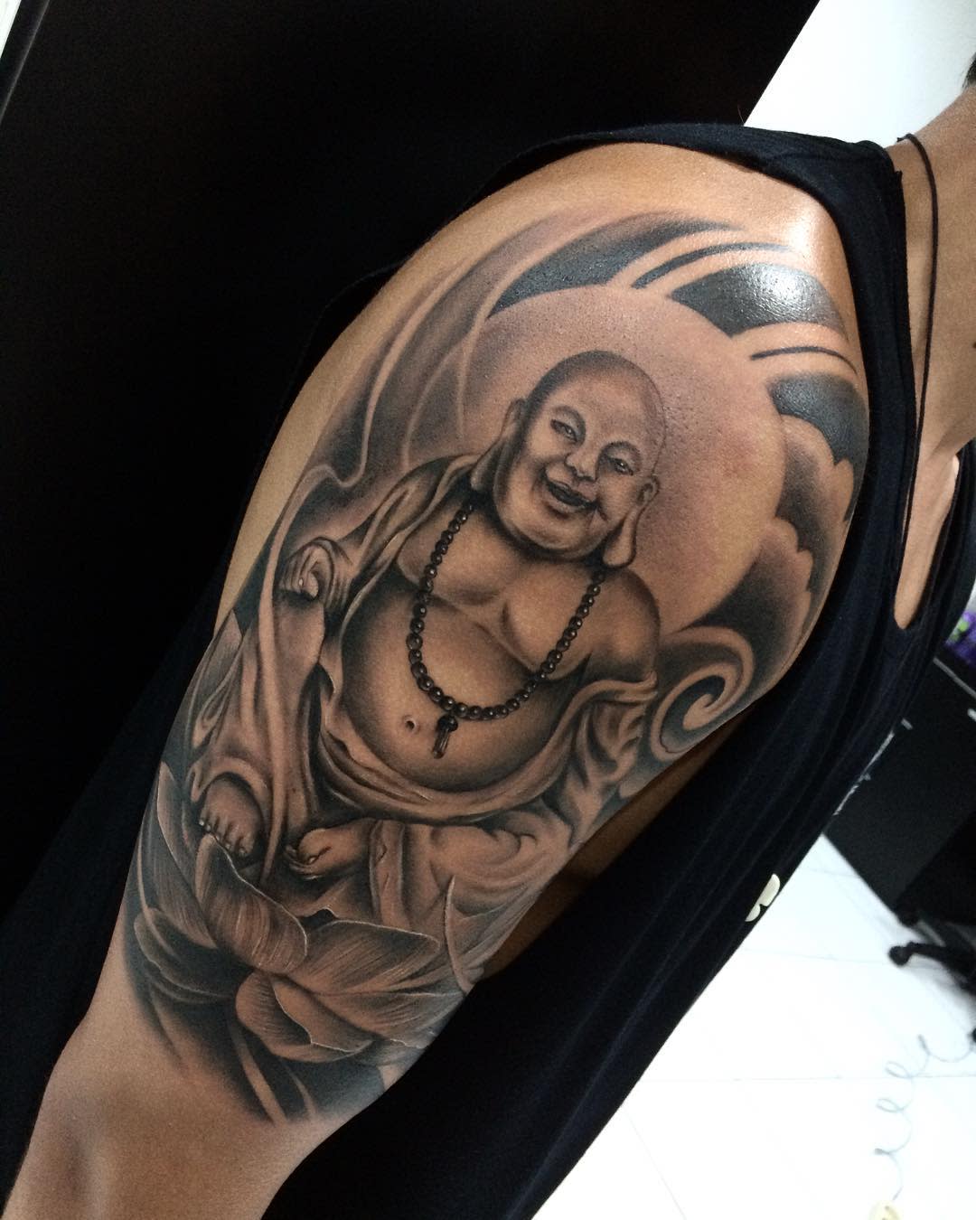 A black and white tattoo of a happy Buddha on an upper arm
