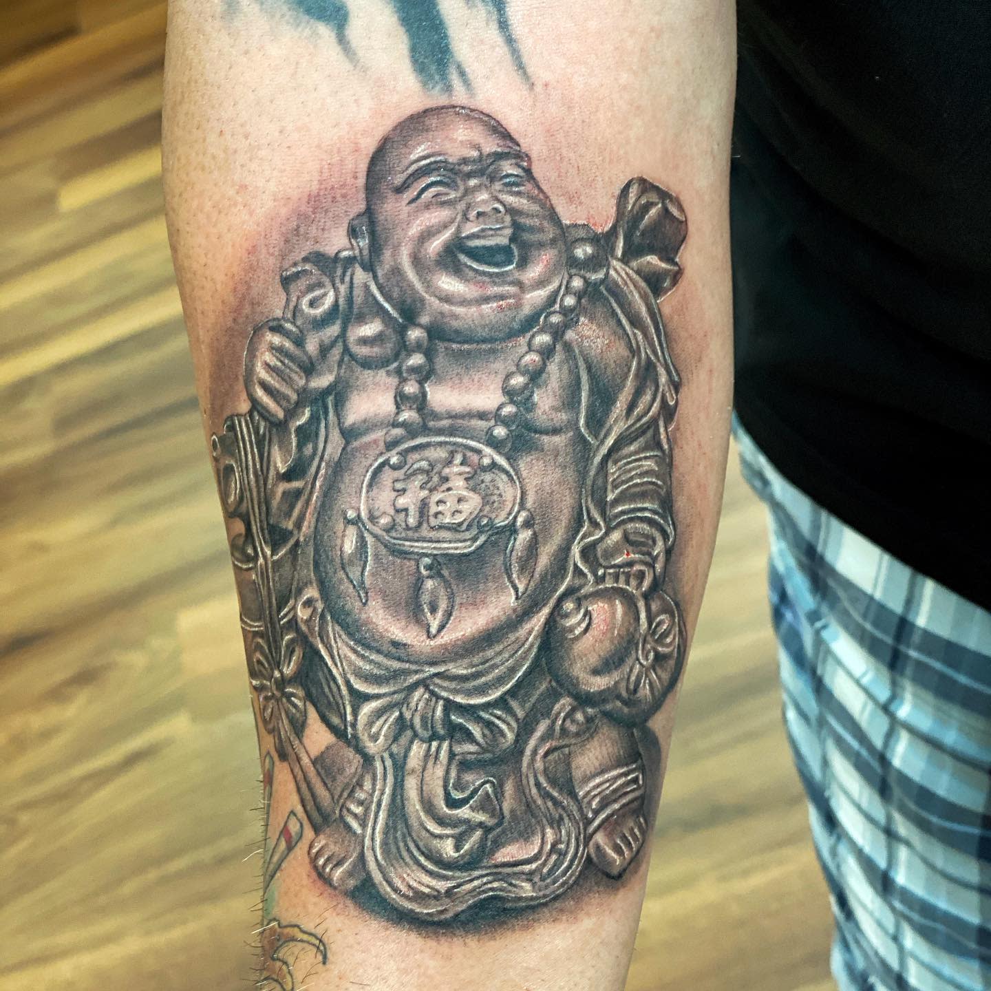 A detailed tattoo of a laughing Buddha on an arm