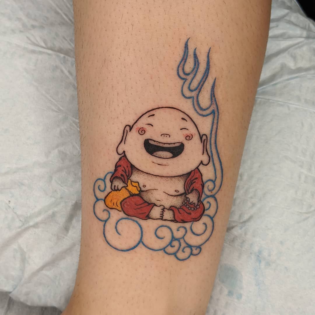 Tattoo of a laughing Buddha in red robes, sitting on a cloud with blue flames