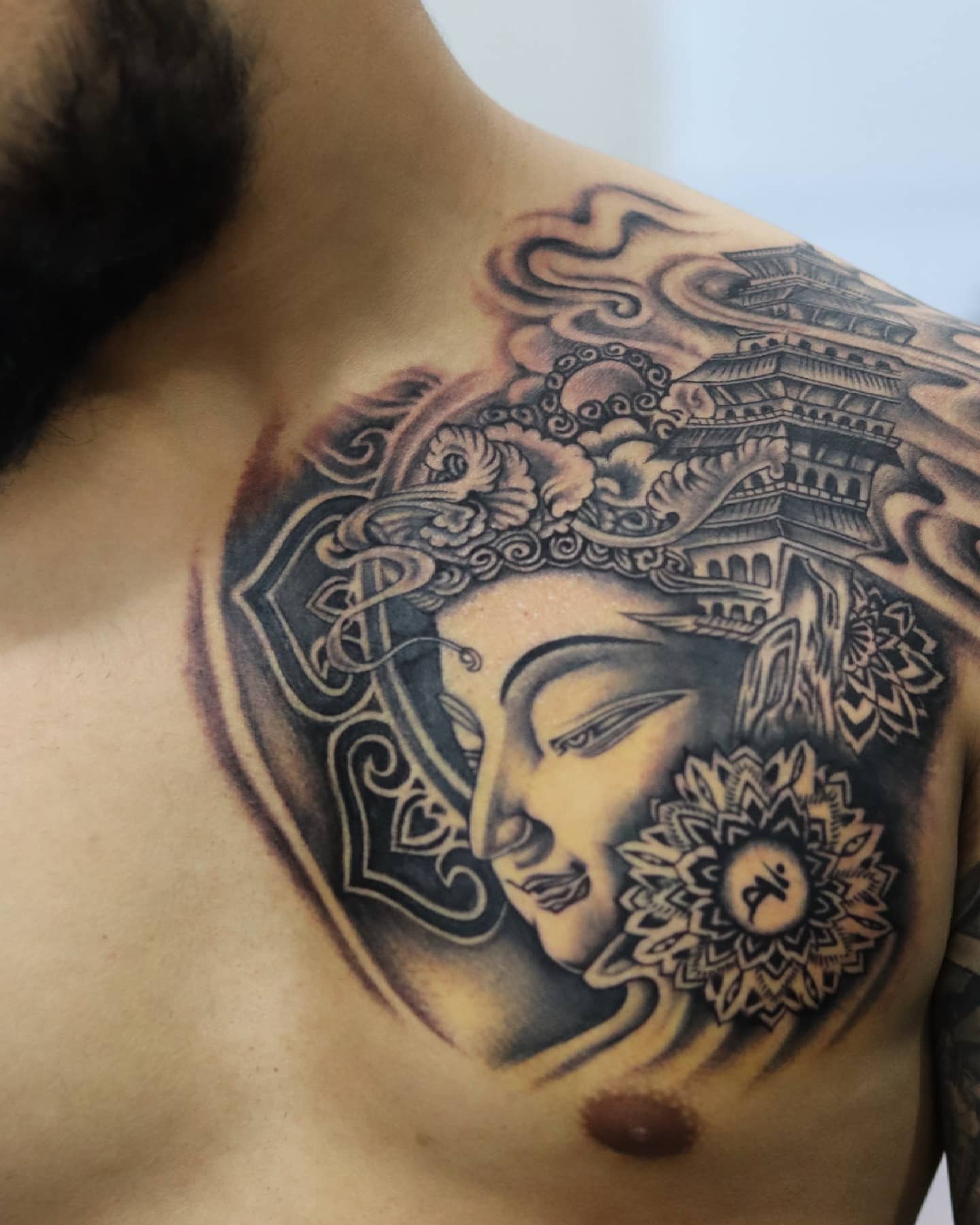 Black and white chest tattoo featuring Buddha enveloped by detailed architectural elements