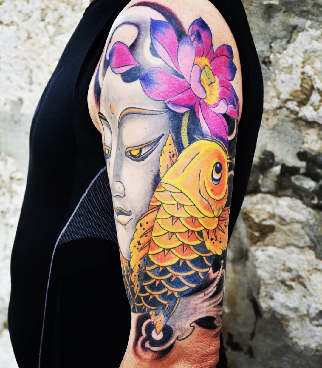 Colorful tattoo of Buddha and koi fish with a pink lotus on an upper arm