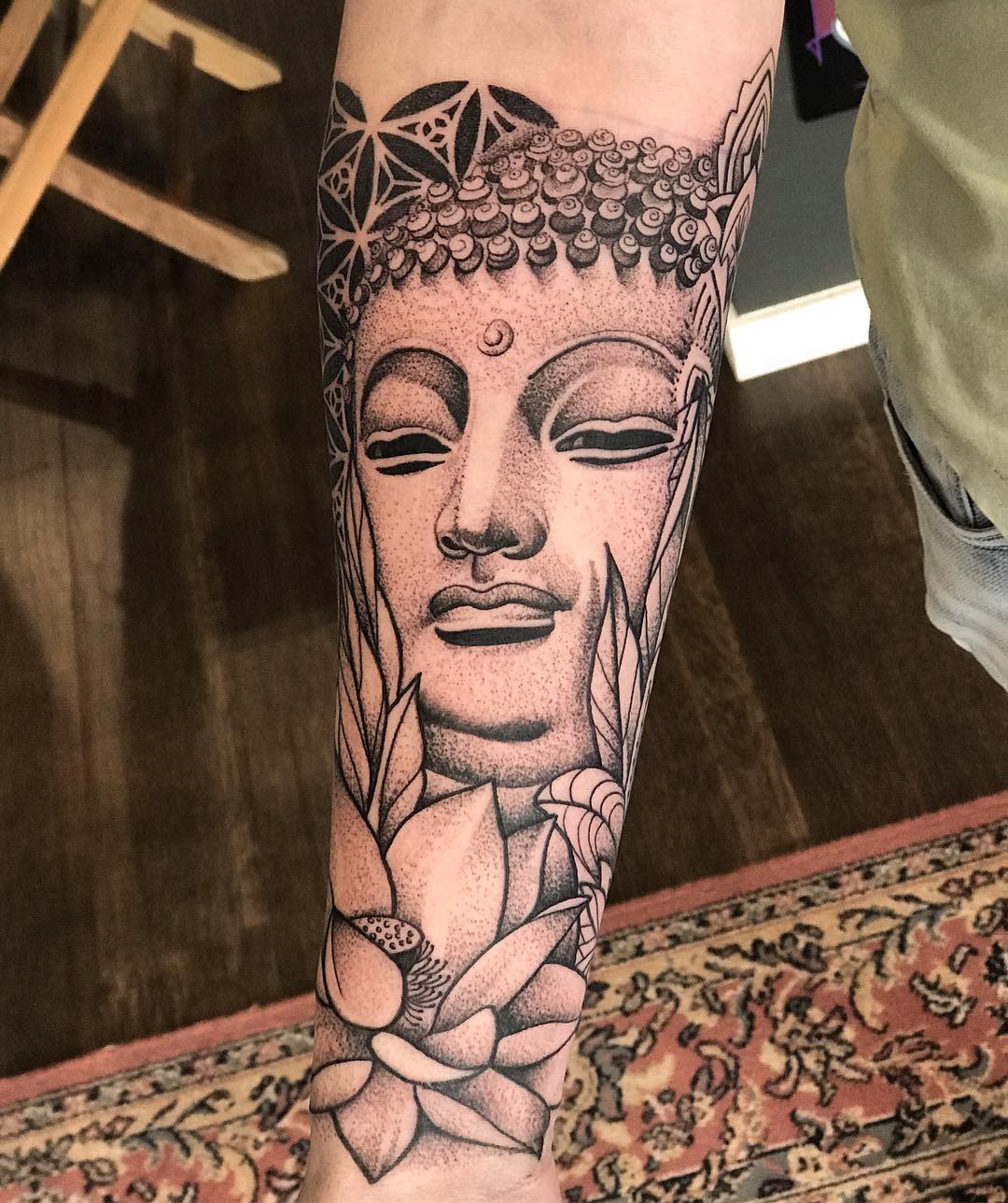 A detailed black and grey Buddha tattoo on a forearm