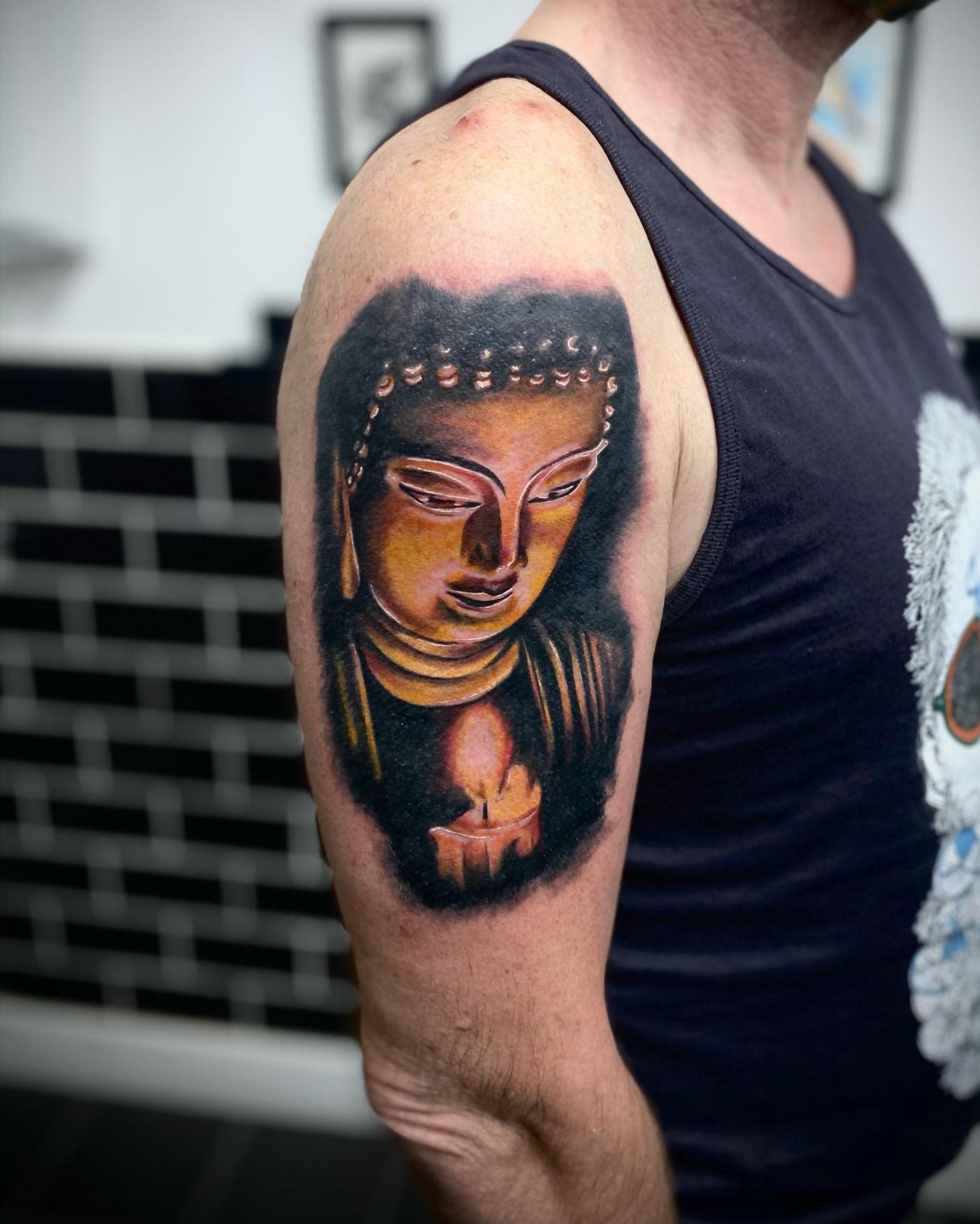 A tattoo of Buddha holding a candle on an upper arm