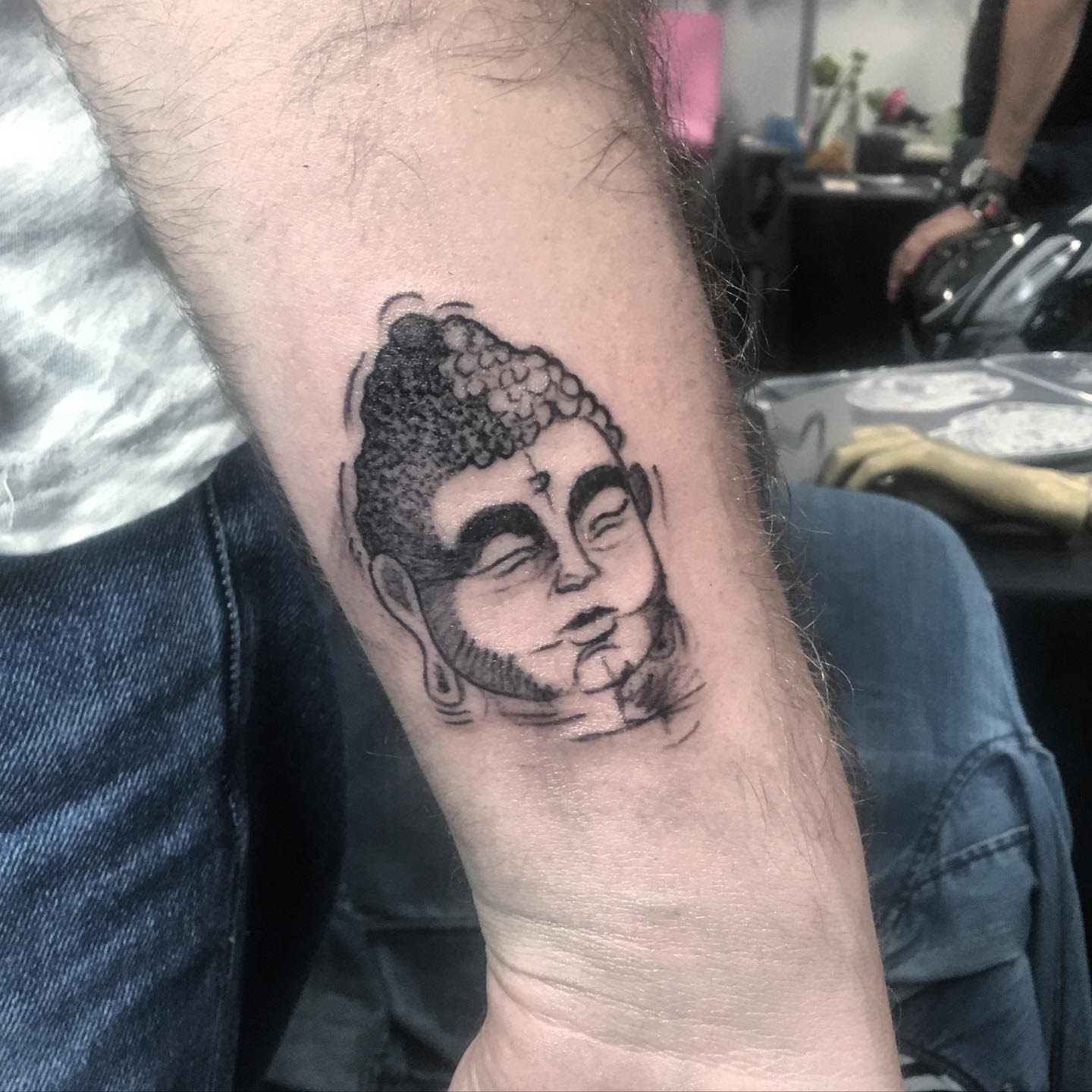 Forearm tattoo of a Buddha head with detailed facial features and intricate hair design