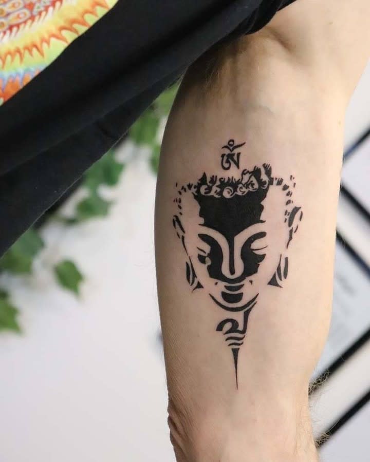 A black Buddha tattoo on an arm with a symbol above the Buddha's head