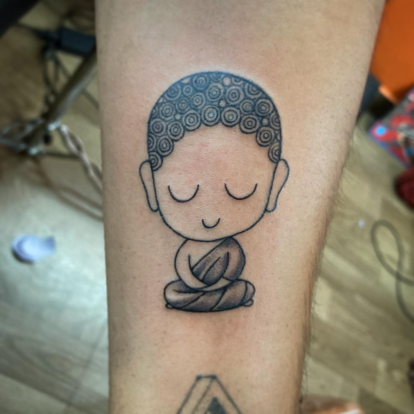 Tattoo of a Buddha in meditation with curly hair and peaceful expression on an arm