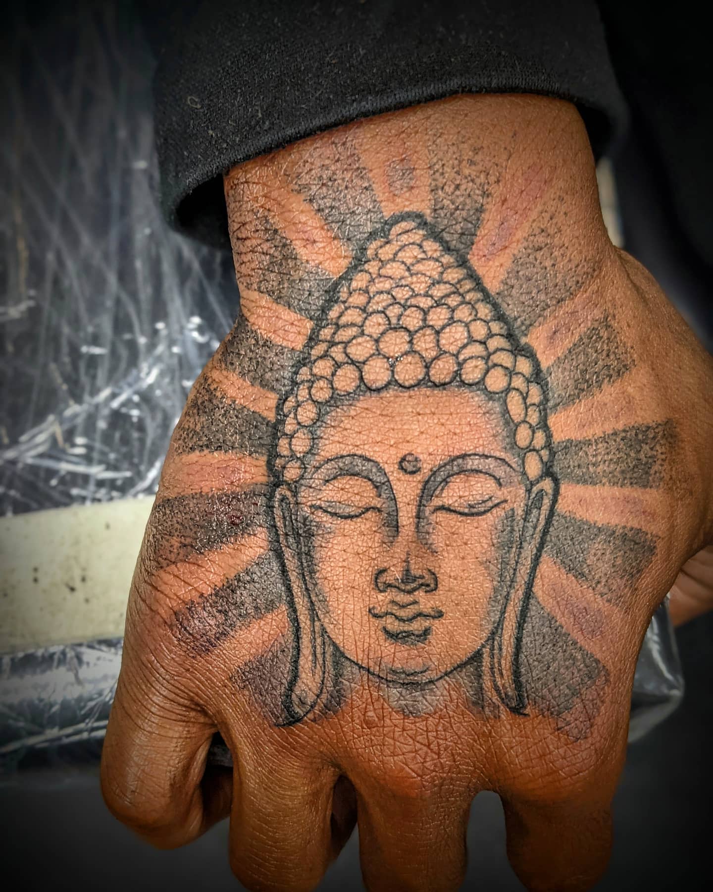 A tattoo of a serene Buddha face with radiant lines on a hand