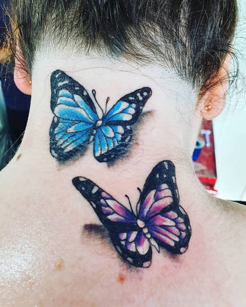 Two vibrantly colored butterflies tattooed on the back of a person's neck and upper back