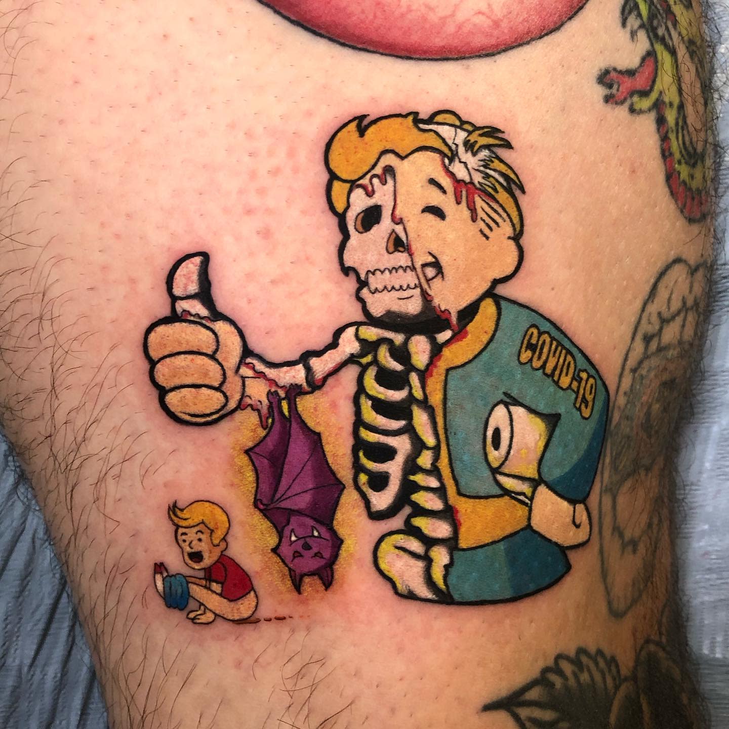 Colorful tattoo featuring a skeleton and a child labeled "COVID-19" on a thigh
