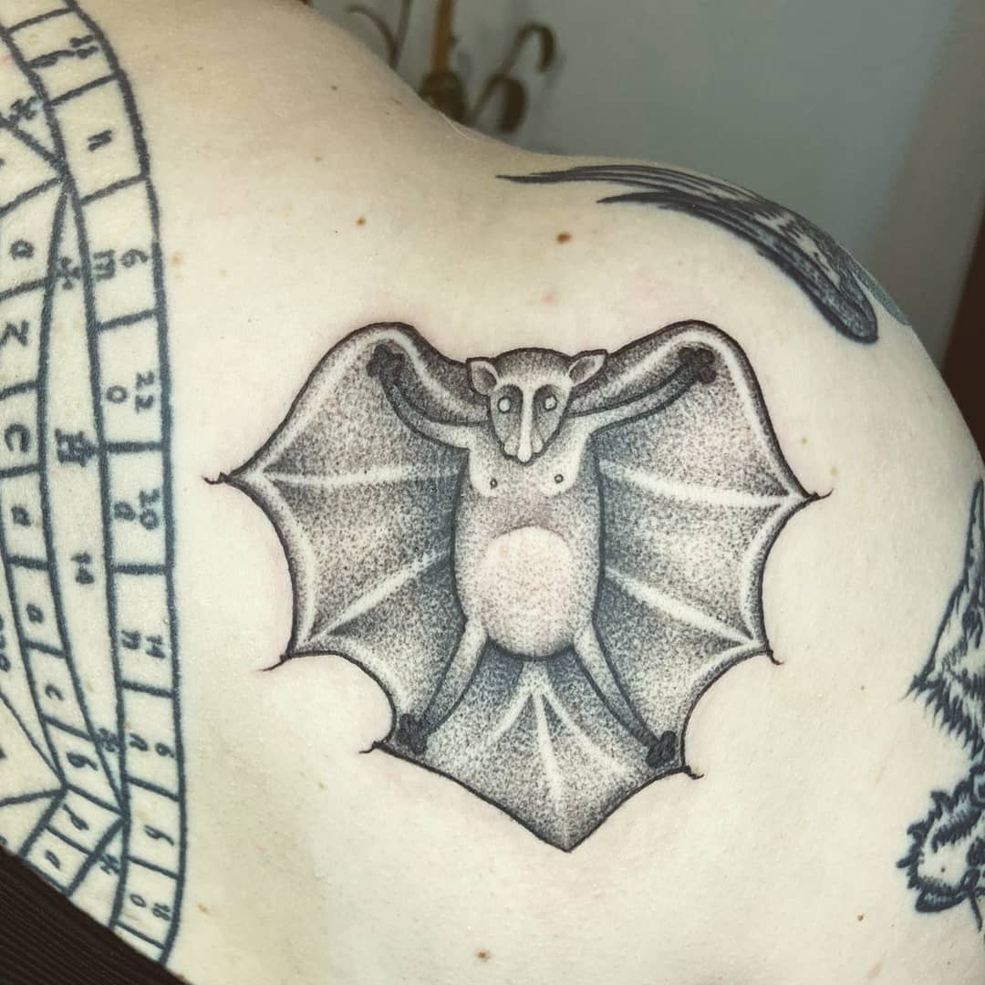 A bat tattoo with outstretched wings on the upper back and shoulder blade