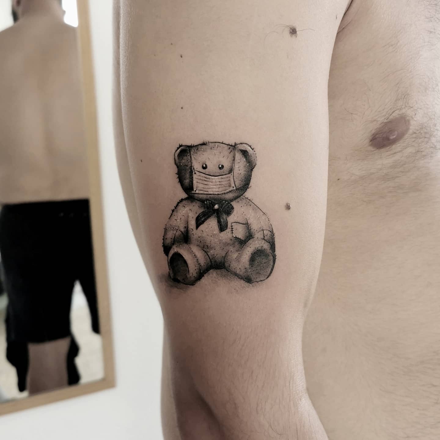 Tattoo of a toy bear with a facemask on a man's upper arm
