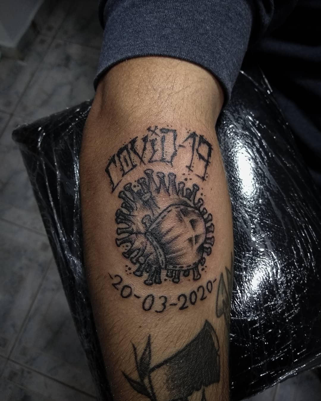 Tattoo of a coronavirus particle with "COVID-19" and "20-03-2020" inked on an arm