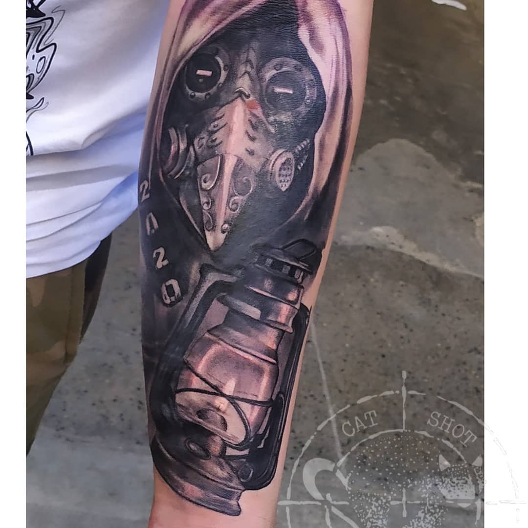 Forearm tattoo of a hooded figure with a gas mask and a lantern, "2020" written on arm