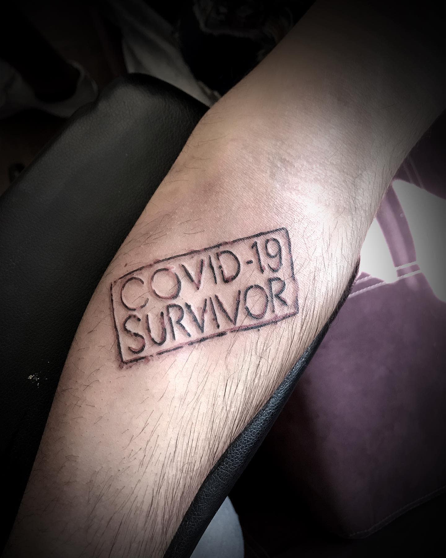 A tattoo on an arm reads "COVID-19 SURVIVOR" in block letters with a rectangle border