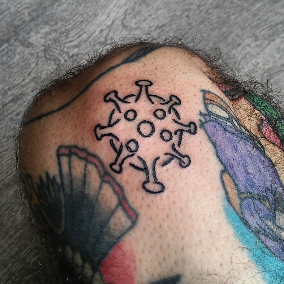 Outline tattoo of a virus particle on a tattooed, lightly hairy knee with colorful ink nearby